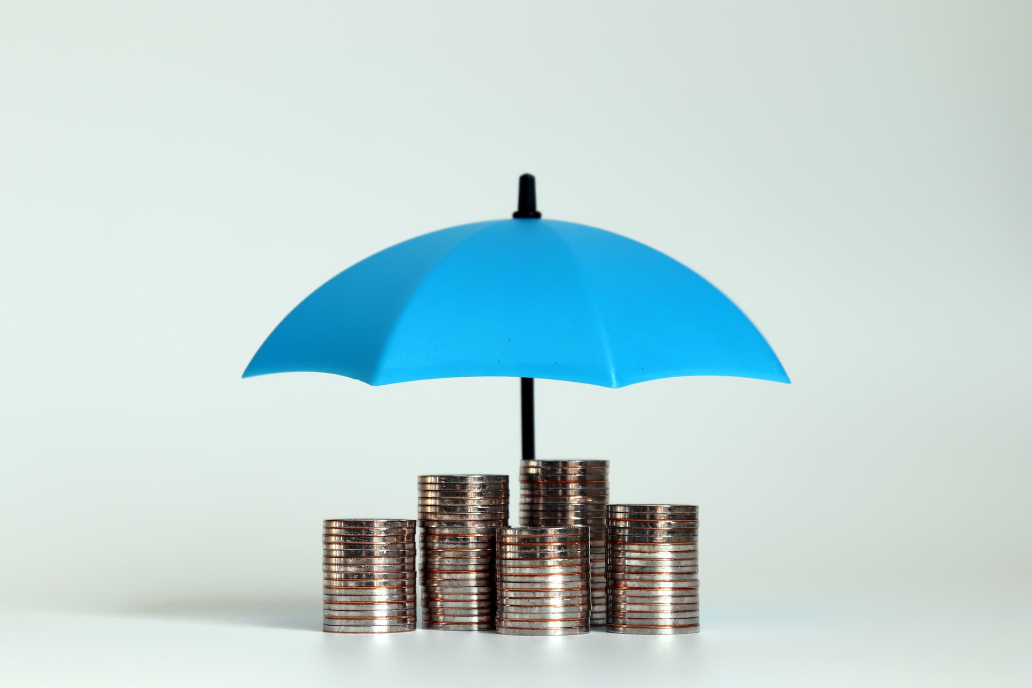 A pile of coins neatly stacked on a table with a mini blue umbrella above them