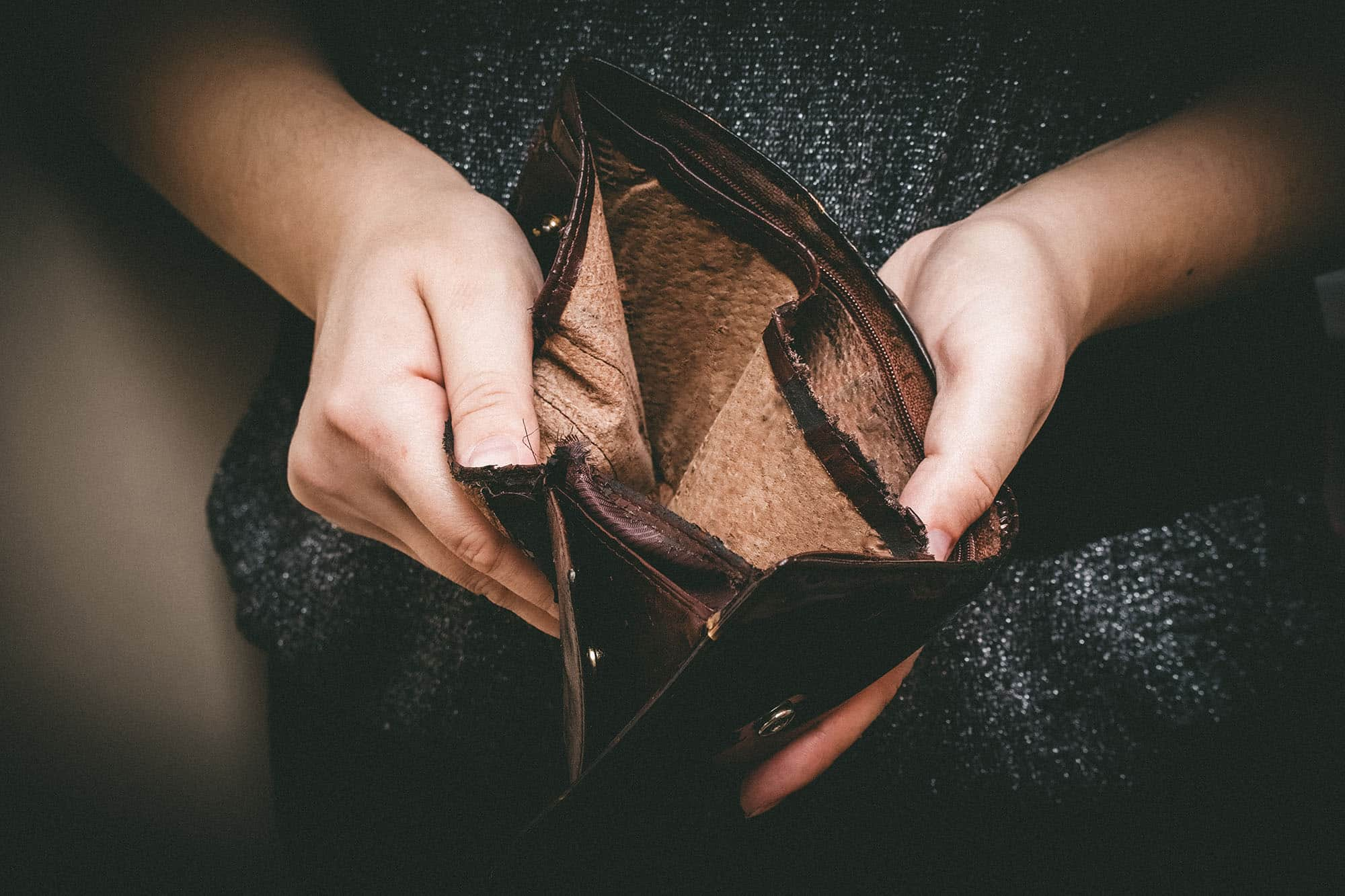 Hands holding old torn wallet with no money inside