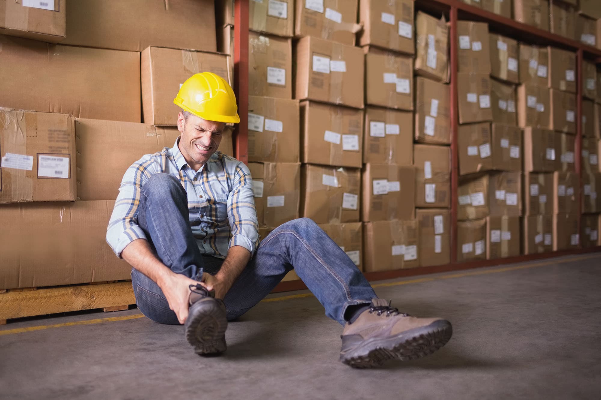 Warehouse worker sitting on ground clutching his ankle after being injured at work