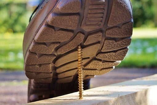 Shoe that is about to step on an exposed nail which will pierce the foot