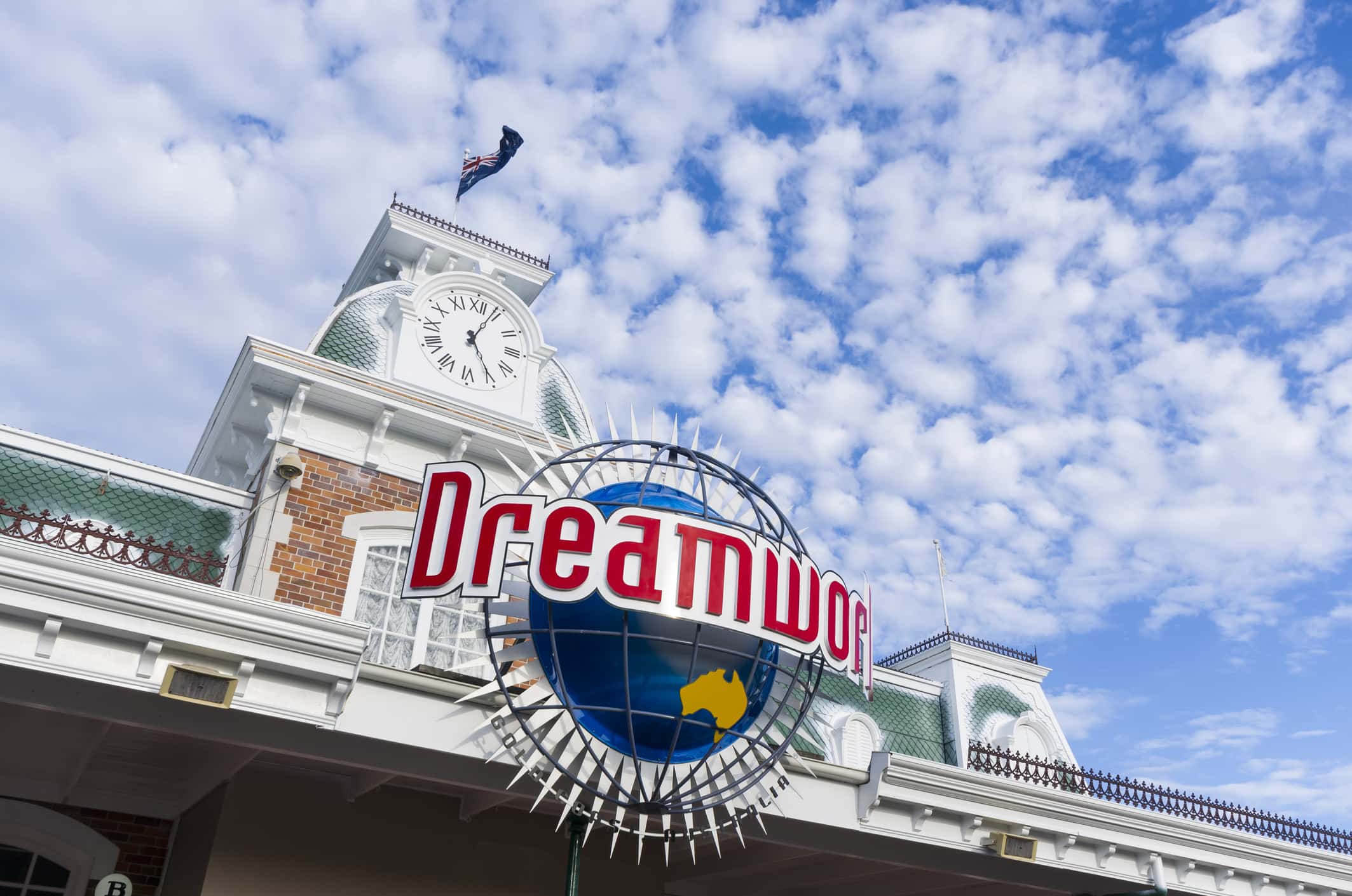 The Facade of Dreamworld Gold Coast entrance building, Australia National flag flying against the beautiful clouds and blue sky.