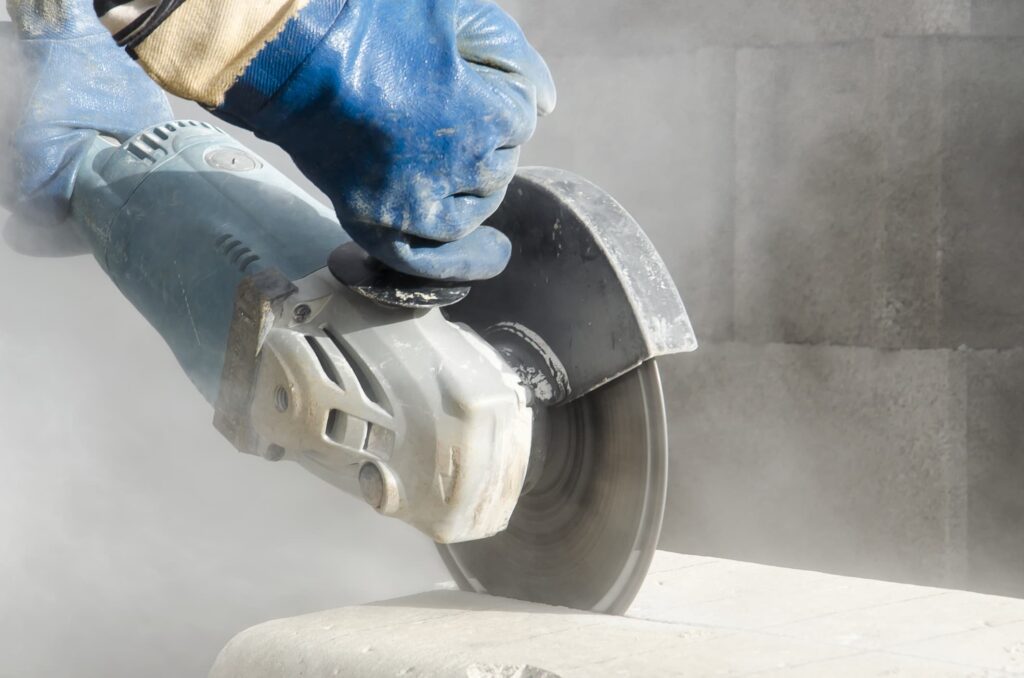 Worker cutting stone with a grinder surrounded by silicosis causing dust