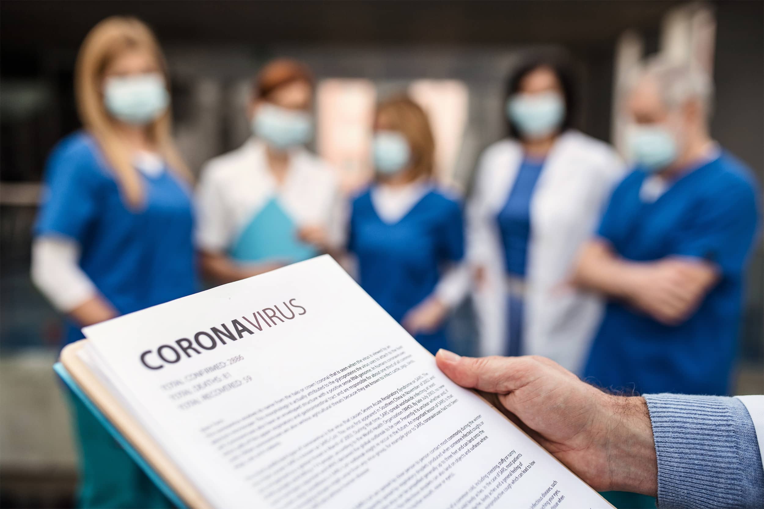 Close up of paperwork with the word coronavirus in bold there are a group of frontline workers in the background