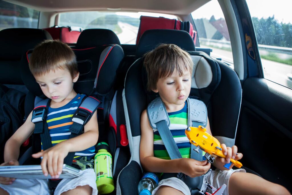 Children sitting in backseat of car paying with toys that may be filled with asbestos that can cause injury