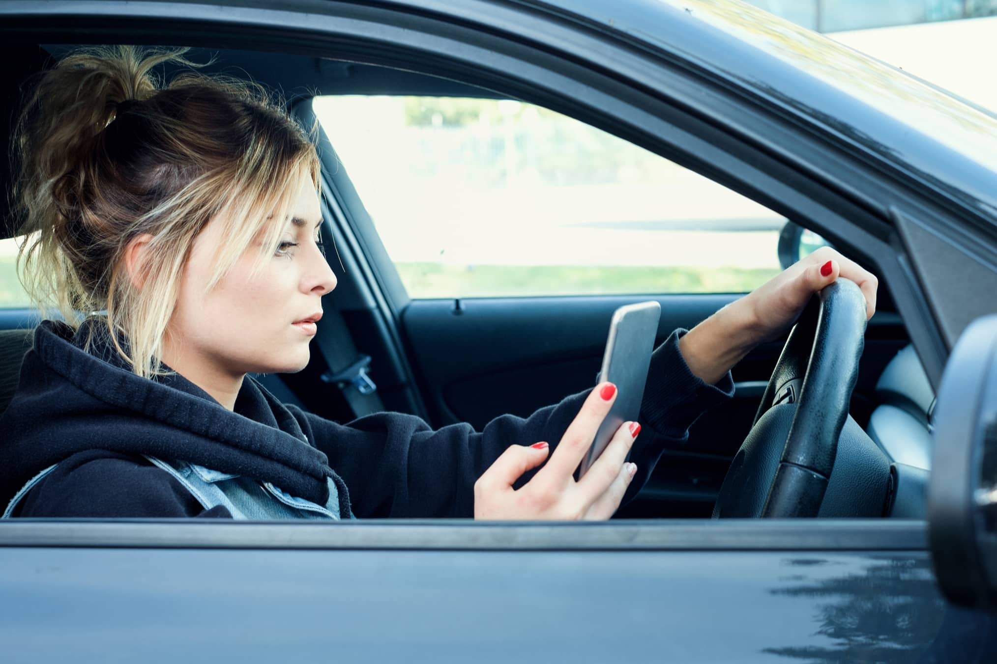 Young female driver driving distracted whilst looking at their mobile phone potentially causing a road accident