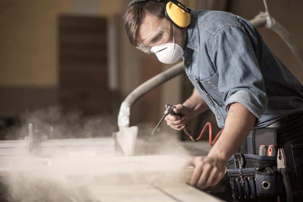 Carpenter sanding wood wearing face mask to protect from occupational disease