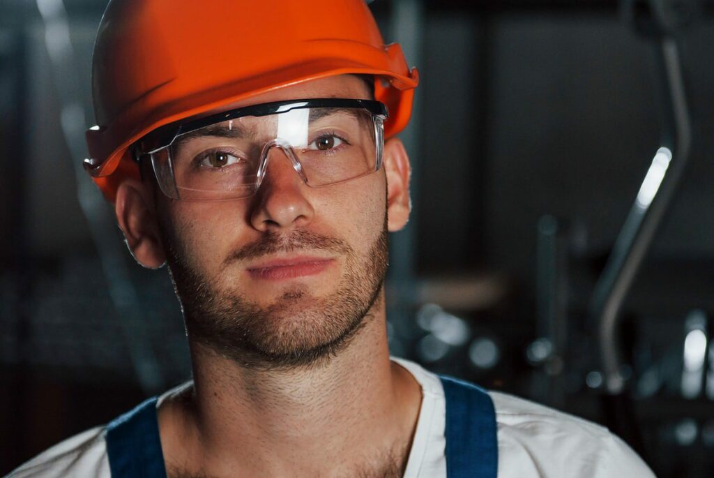 Young male construction worker wearing orange hardhat and safety goggles