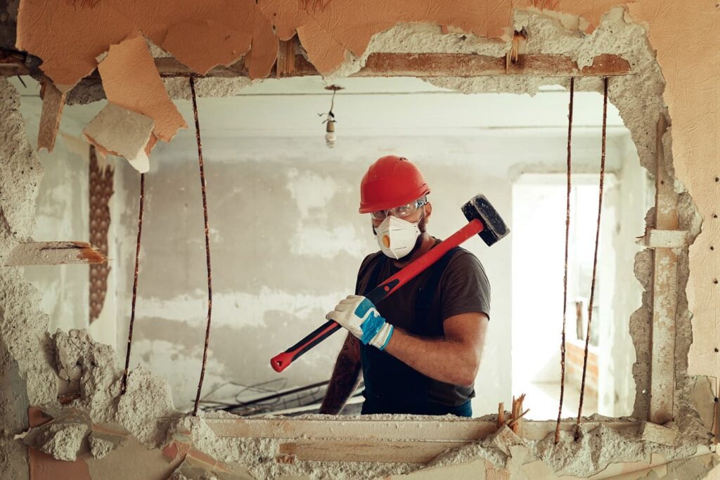 Builder with a hammer in hands demolishing old home